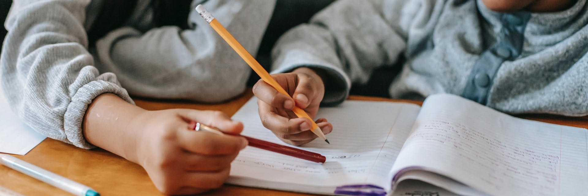 Two students sit at a desk together working on writing prompts for kids.