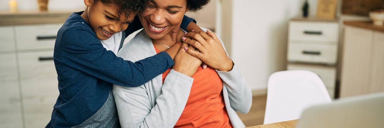 Happy mother and child hugging at their desk in front of their laptop, after purchasing a Prodigy Membership.
